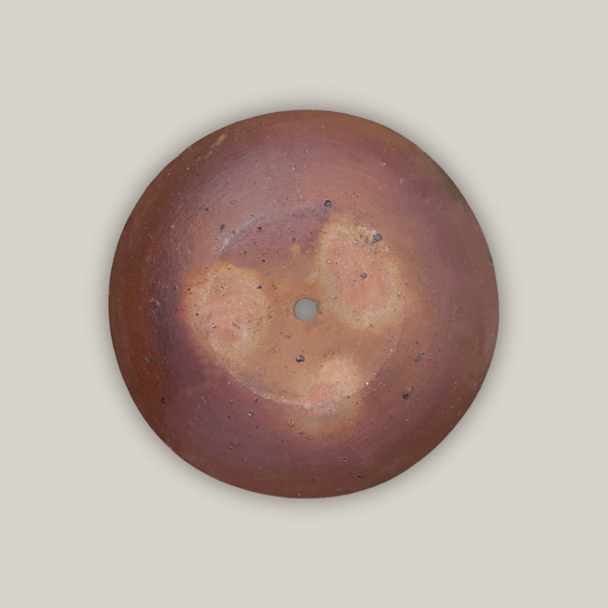 Underside of the Iron Clay Rustic Style Wide Bowl, showing natural fire-mottled clay tones and a central drainage hole against a deep rust-brown base.