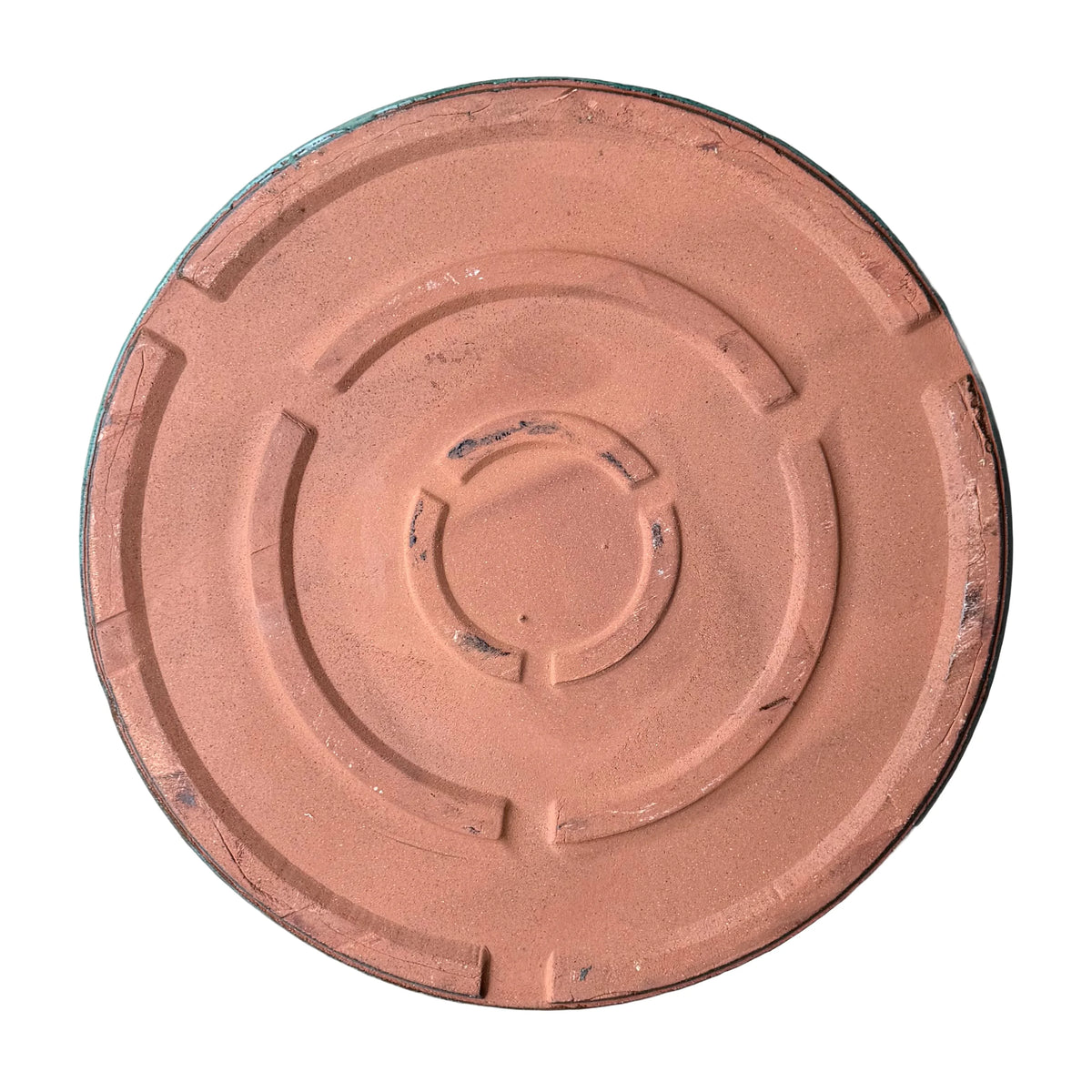 Underside of a round teal ceramic plant saucer, showing an unglazed terracotta base with raised concentric ring feet and a thin edge of teal glaze around the rim