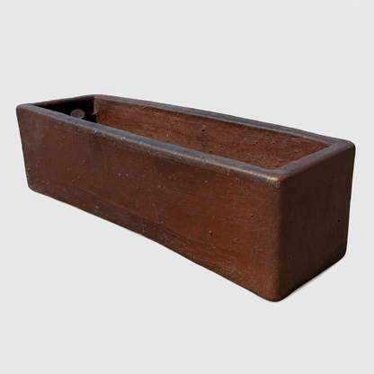 A rustic rectangular planter made of dark brown textured clay, shown at an angle on a light gray background.