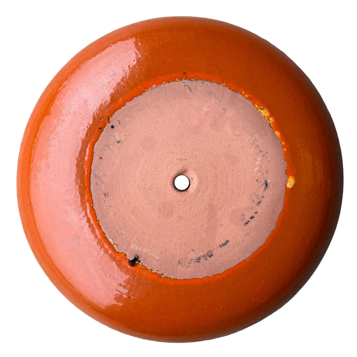 Underside of an atomic orange ceramic succulent bowl, showing an unglazed terracotta base with a central drainage hole, framed by a ring of glossy bright orange glaze