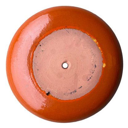 Underside of an atomic orange ceramic succulent bowl, showing an unglazed terracotta base with a central drainage hole, framed by a ring of glossy bright orange glaze