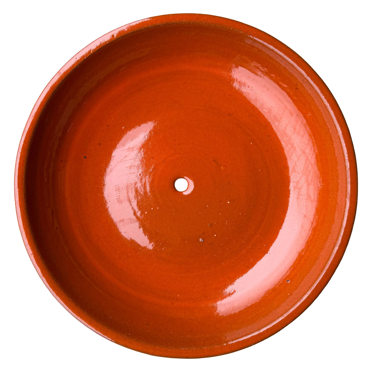 Top-down view inside an atomic orange ceramic succulent bowl, with a smooth, high-gloss orange glaze, faint concentric rings, and a single drainage hole in the center