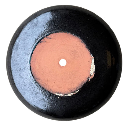Underside of a black ceramic succulent bowl, showing an unglazed terracotta base with a central drainage hole, surrounded by a band of glossy black glaze