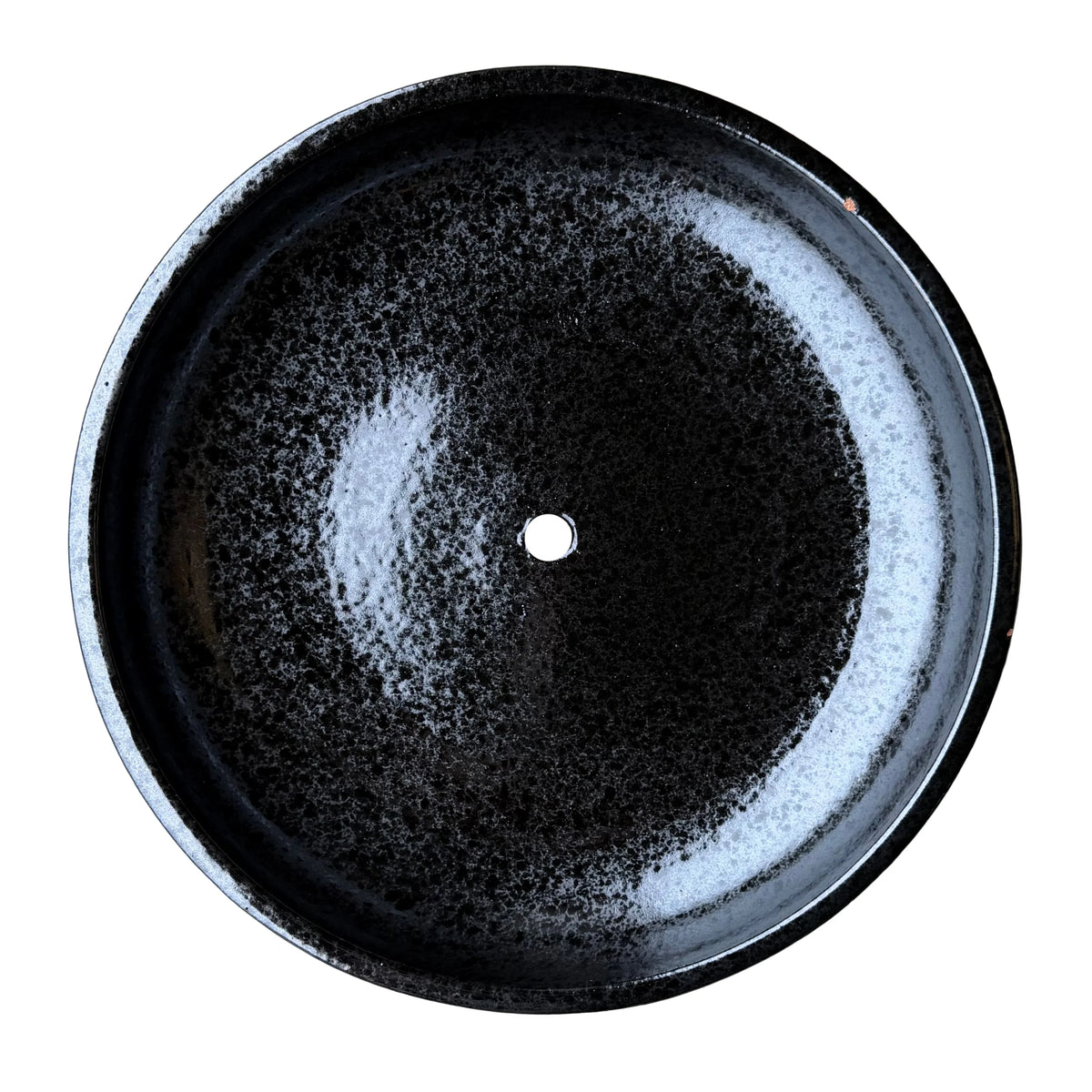 Top-down view inside a black ceramic succulent bowl, with a glossy black glaze finely mottled with grey speckles and a single drainage hole in the center
