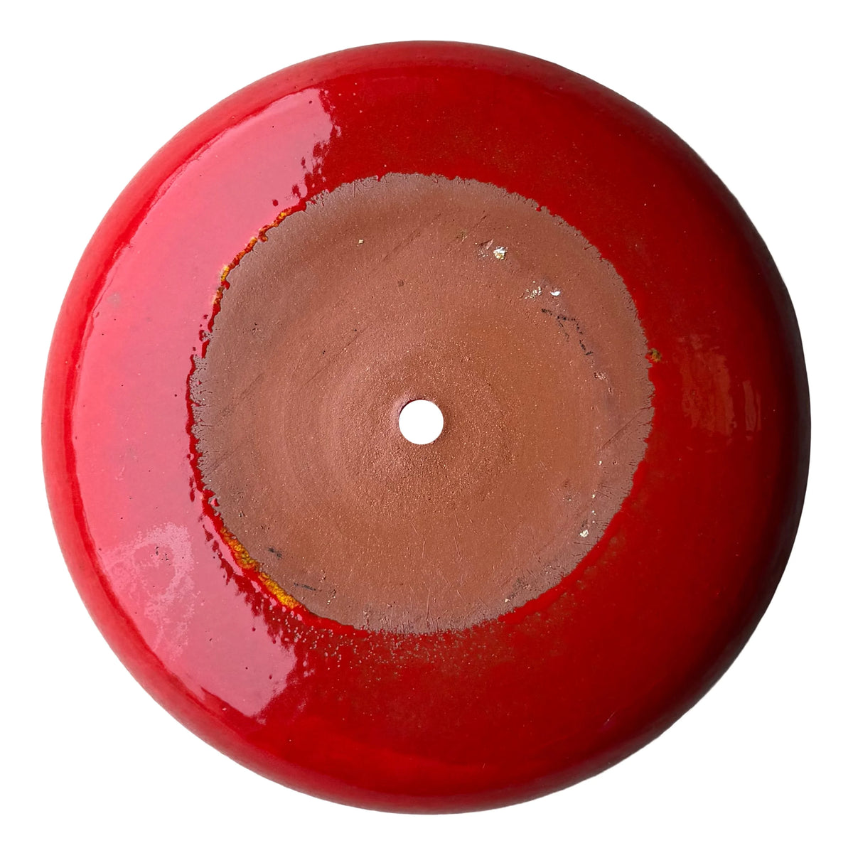 Underside of a bright red ceramic succulent bowl, showing an unglazed terracotta base with a central drainage hole, ringed by glossy red glaze