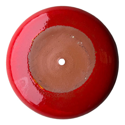 Underside of a bright red ceramic succulent bowl, showing an unglazed terracotta base with a central drainage hole, ringed by glossy red glaze