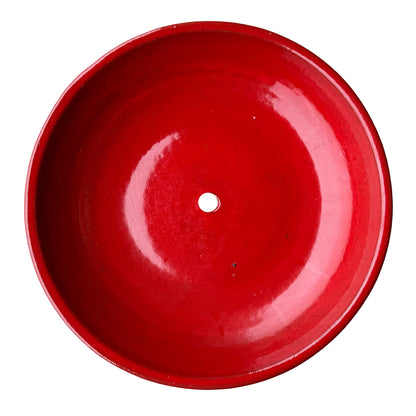 Top-down view inside a bright red ceramic succulent bowl, with a smooth high-gloss red glaze, a raised rim and a single drainage hole in the center