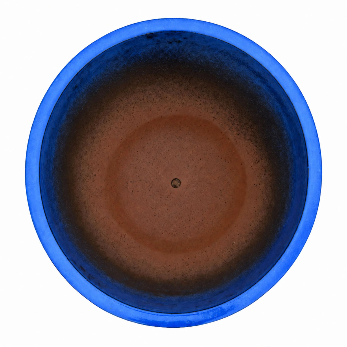 Top-down view of a blue tapered planter, with a glossy cobalt-blue rim and upper walls that deepen to dark blue and fade into a terracotta-brown floor with a small drainage hole