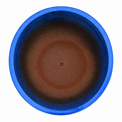 Top-down view of a blue tapered planter, with a glossy cobalt-blue rim and upper walls that deepen to dark blue and fade into a terracotta-brown floor with a small drainage hole
