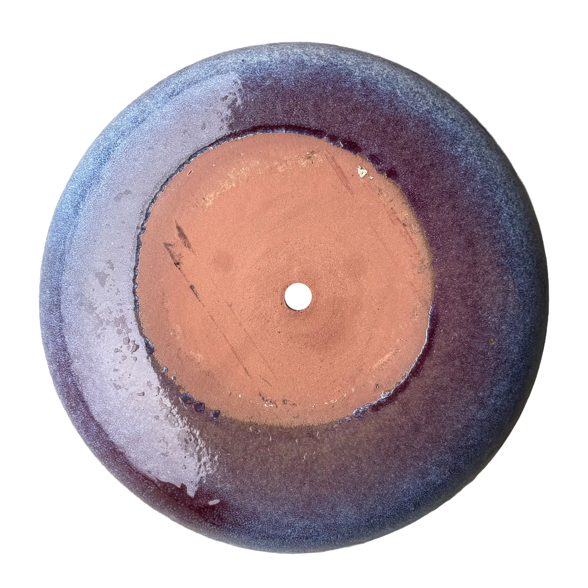 Underside of a falling purple ceramic succulent bowl, showing an unglazed terracotta base with a central drainage hole, ringed by plum glaze that fades to speckled periwinkle at the edge