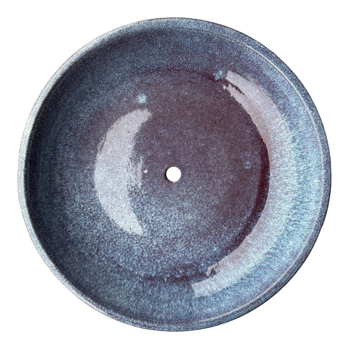 Top-down view inside a falling purple ceramic succulent bowl, where a flecked blue glaze deepens to dusky plum around a single drainage hole
