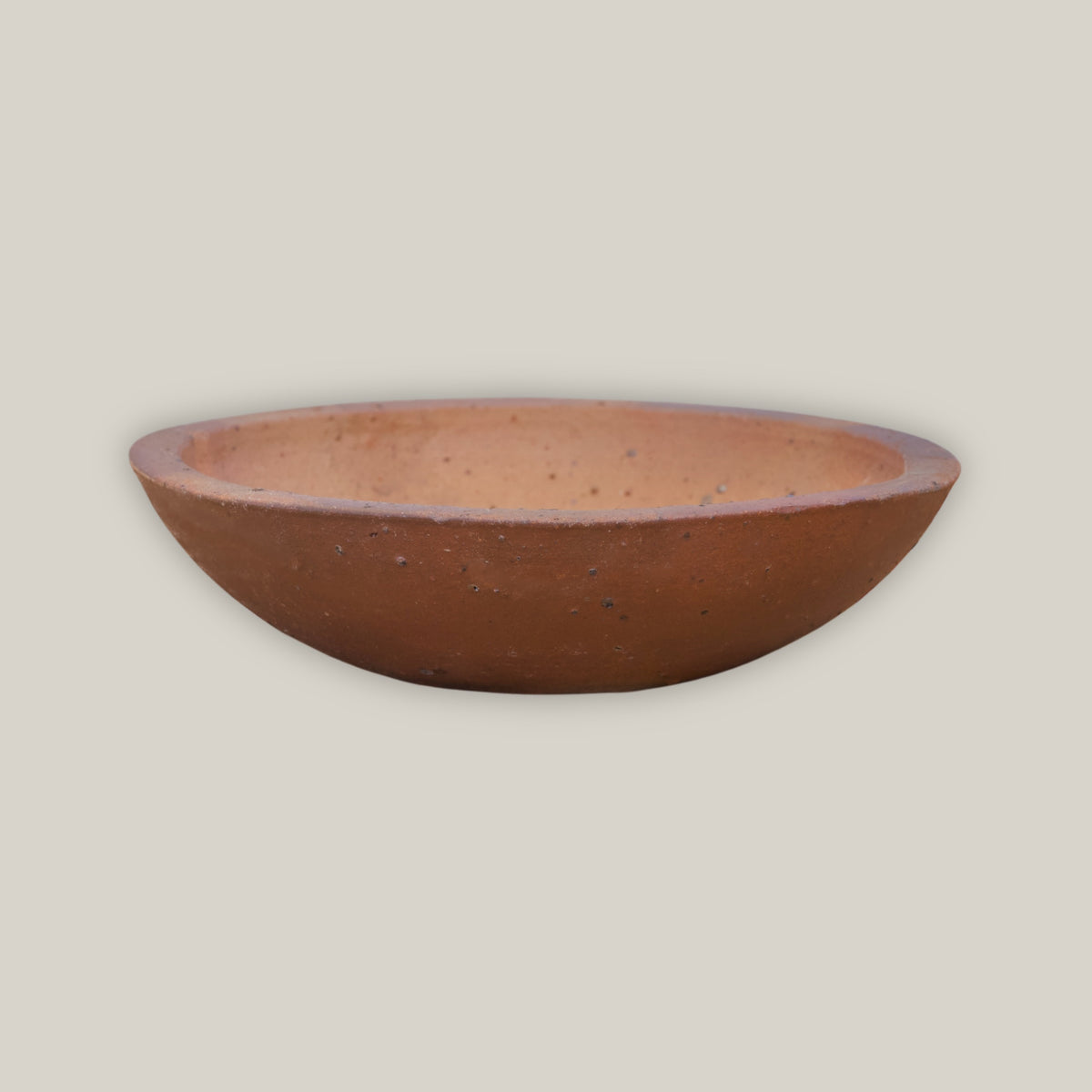 An Iron Clay Rustic Style Wide Bowl tilted to reveal its warm terracotta interior, sitting low and wide on natural unglazed clay with a subtly rolled rim.
