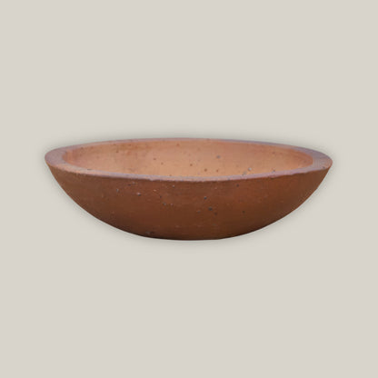 An Iron Clay Rustic Style Wide Bowl tilted to reveal its warm terracotta interior, sitting low and wide on natural unglazed clay with a subtly rolled rim.