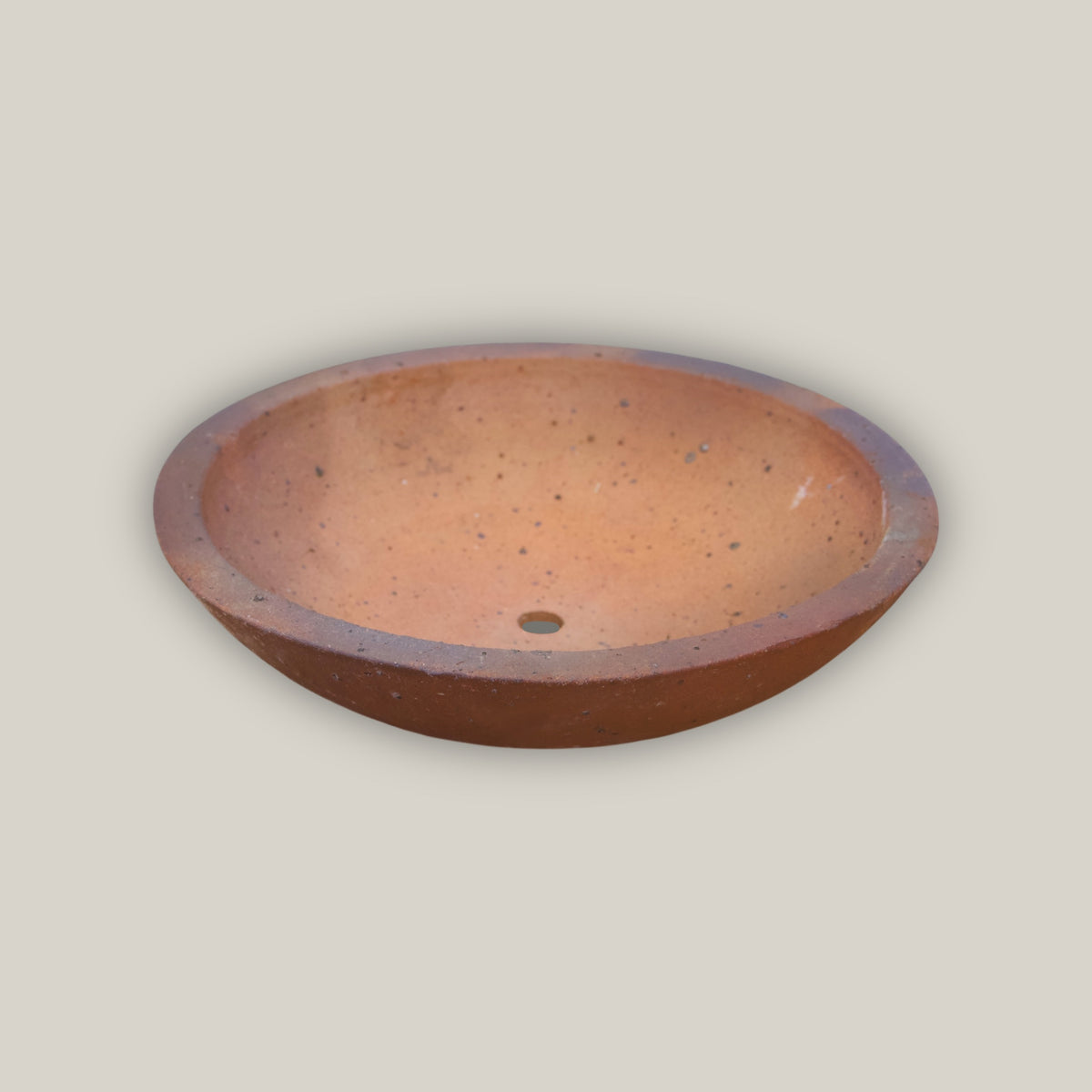 An Iron Clay Rustic Style Wide Bowl seen at a low angle, its shallow terracotta basin and small drainage hole set against a smooth, unglazed rust-brown clay exterior with a subtly rolled rim.
