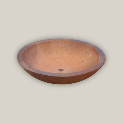 An Iron Clay Rustic Style Wide Bowl seen at a low angle, its shallow terracotta basin and small drainage hole set against a smooth, unglazed rust-brown clay exterior with a subtly rolled rim.