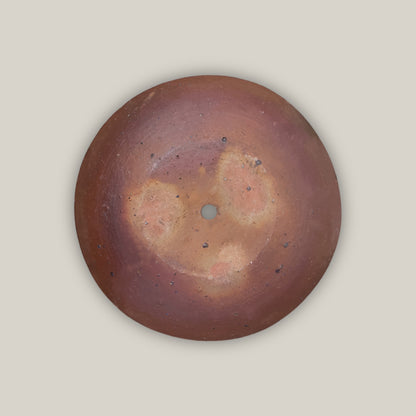 Underside of the Iron Clay Rustic Style Wide Bowl, showing natural fire-mottled clay tones and a central drainage hole against a deep rust-brown base.