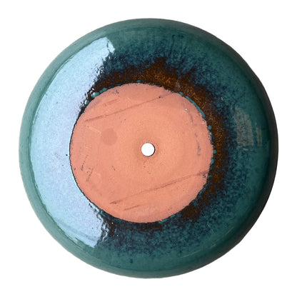 Underside of a jade ceramic succulent bowl, with an unglazed terracotta base, a drainage hole, and a rust-brown ring blending into green.