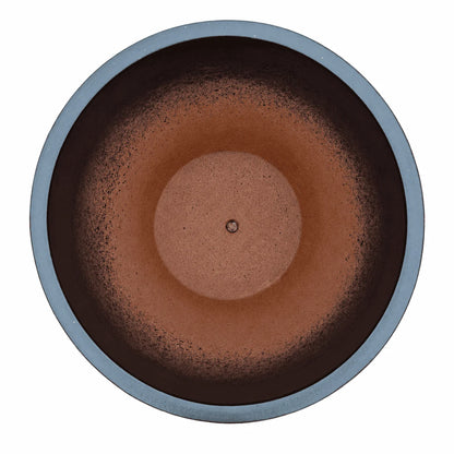Top-down view of a matte black tapered round ceramic planter, with dark inner walls that fade into a terracotta interior with a raised circular centre and a small drainage hole
