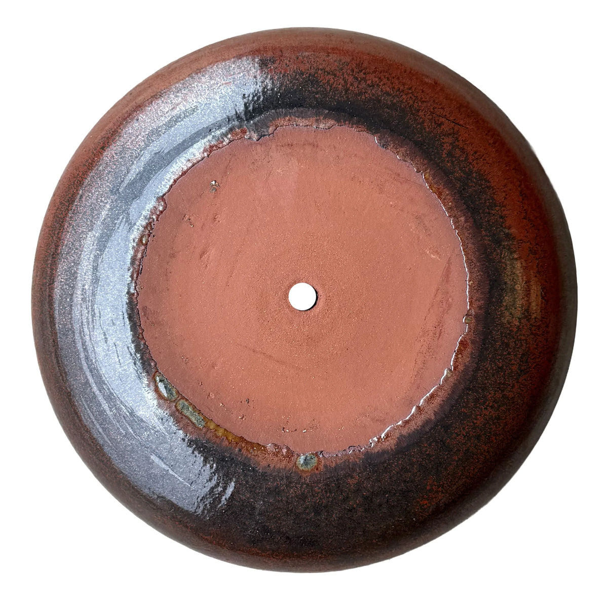 Underside of an oxide ceramic succulent bowl, showing an unglazed terracotta base and drainage hole ringed by rust and black glaze