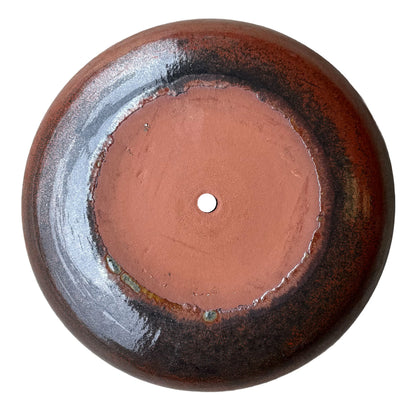 Underside of an oxide ceramic succulent bowl, showing an unglazed terracotta base and drainage hole ringed by rust and black glaze