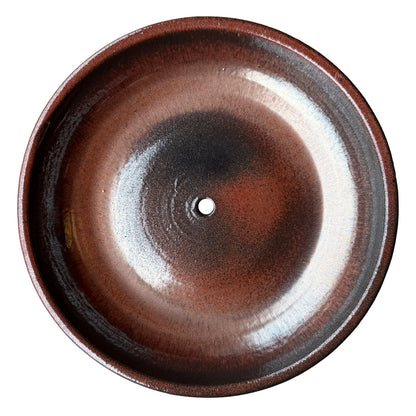 Top-down view inside an oxide ceramic succulent bowl, showing a glossy rust-red glaze that darkens to dark gray around a single central drainage hole