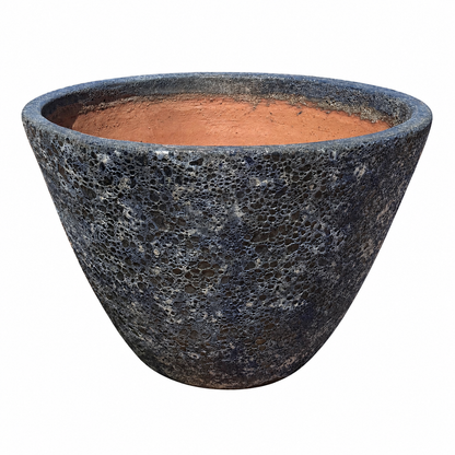 A Relic Rust/Metal Blue Giant Cone Ceramic Planter tilted forward to show its warm terracotta interior, its exterior covered in a deeply pitted, volcanic-textured charcoal-blue finish.