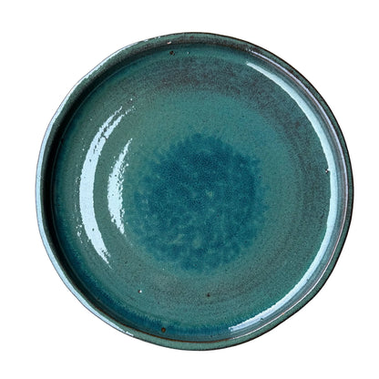 Top-down view of a round teal ceramic plant saucer with a glossy speckled teal-green glaze that pools into deeper blue at the center, framed by a low raised rim