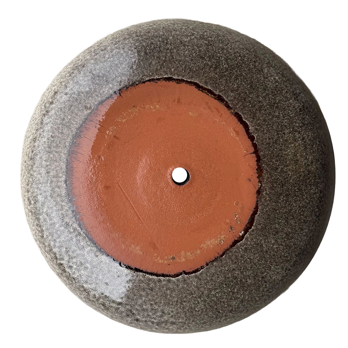 Underside of a speckle black ceramic succulent bowl, showing a terracotta clay base with a central drainage hole, ringed by a speckled gray-brown glaze
