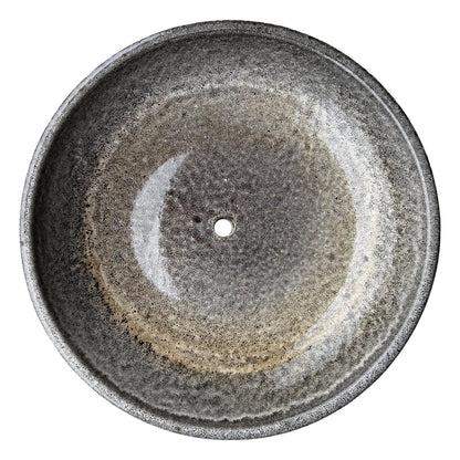 Top-down view inside a speckle black ceramic succulent bowl, where a mottled grey glaze shifts to a golden-tan ring and a darker speckled center around the drainage hole