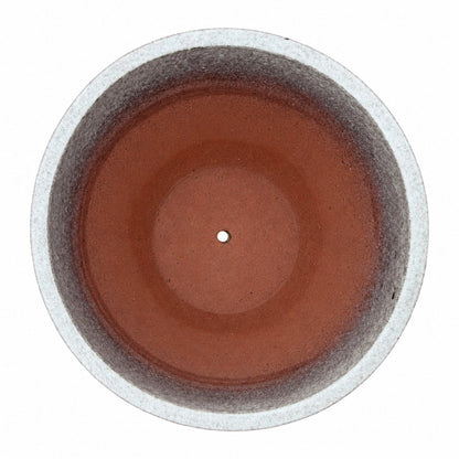 Top-down view of a speckle black tapered round ceramic planter, with a pale speckled rim and inner walls that shade from mottled grey into a terracotta-red floor with a small central drainage hole
