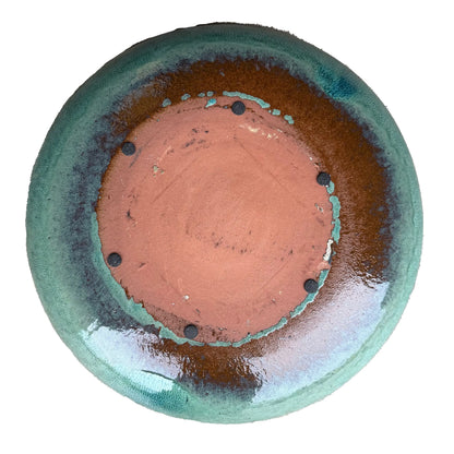 Underside of a teal ceramic bird bath bowl, with an unglazed terracotta base, a rust-brown glaze ring, and six small dark pads.