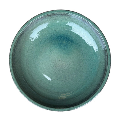 Top-down view of a teal ceramic bird bath bowl, showing a wide glossy basin with deeper blue pooling and a dark-flecked rim.
