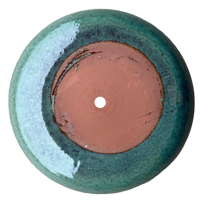 Underside of a teal ceramic succulent bowl, showing an unglazed terracotta base with a centered drainage hole, ringed by speckled teal glaze that deepens to blue-green near the foot
