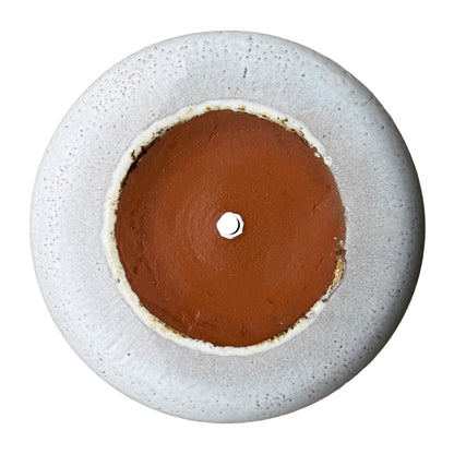 Underside of a white ceramic succulent bowl, showing an unglazed terracotta clay base, a centered drainage hole and a speckled white glazed outer edge
