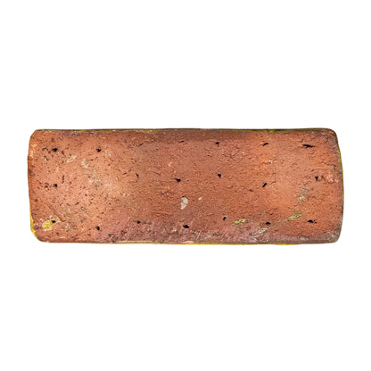 Unglazed terracotta underside of a yellow ceramic pot foot, with a rough, pitted clay surface that sits on the ground.