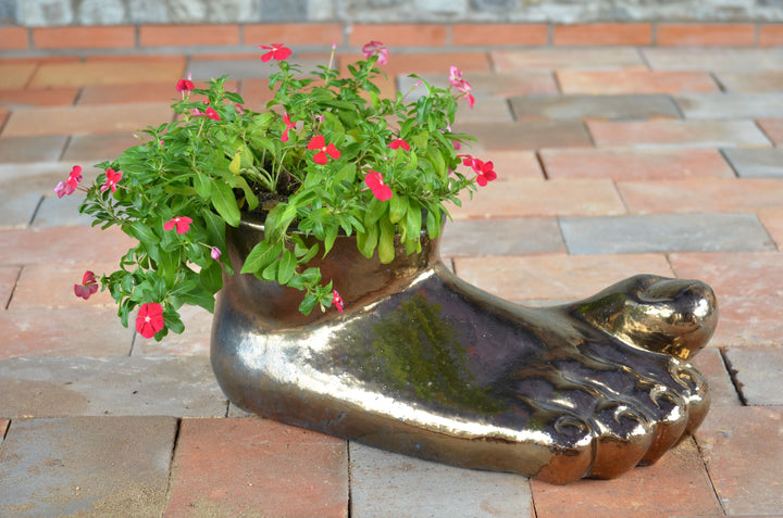 Image of a metallic right foot planter with a plant in it.